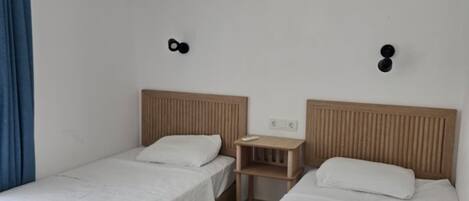 A room with two beds, a small table, and a wall-mounted air conditioner.