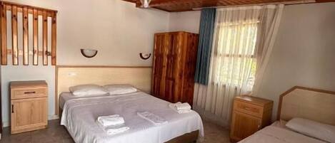 A room with two beds, wooden ceiling, and a window with curtains.