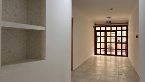 Un pasillo con piso de baldosas, una pared blanca con una sección moteada y una puerta de madera con paneles de vidrio.