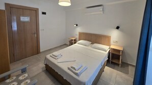 Habitación de hotel con cama, mesitas de noche, cabecera de madera, lámpara en el techo, equipo de aire acondicionado y una puerta con un cartel.