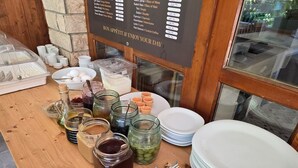 Un bufé de desayuno con diversas opciones de comida y salsas, un cartel de menú y platos blancos apilados.