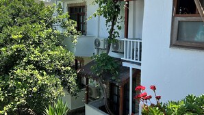Un edificio residencial con balcón, equipos de aire acondicionado y un jardín con diversas plantas.