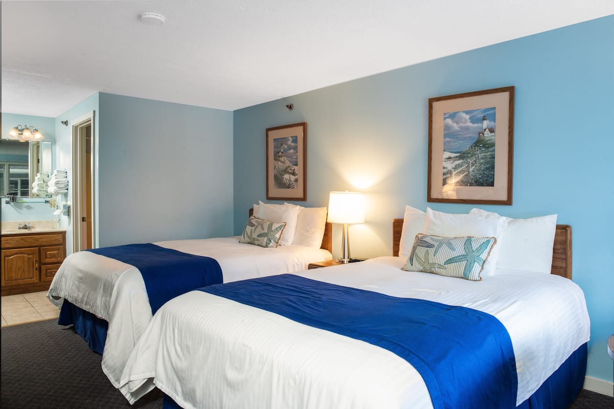 A hotel room with two beds, a bathroom, and a view of the ocean.