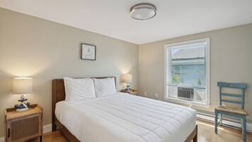 Een slaapkamer met een groot bed, twee nachtkastjes met lampen, een raam met jaloezieën en een stoel.
