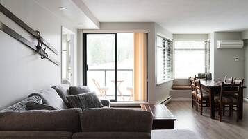 A modern living room with a sofa, dining table, and chairs. There is a sliding glass door leading to a balcony.