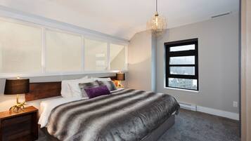 Een slaapkamer met een groot bed, een nachtkastje met een lamp, een raam met uitzicht en een hangende lamp.