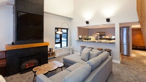 Una sala de estar moderna con chimenea, un amplio sofá modular y una cocina al fondo.