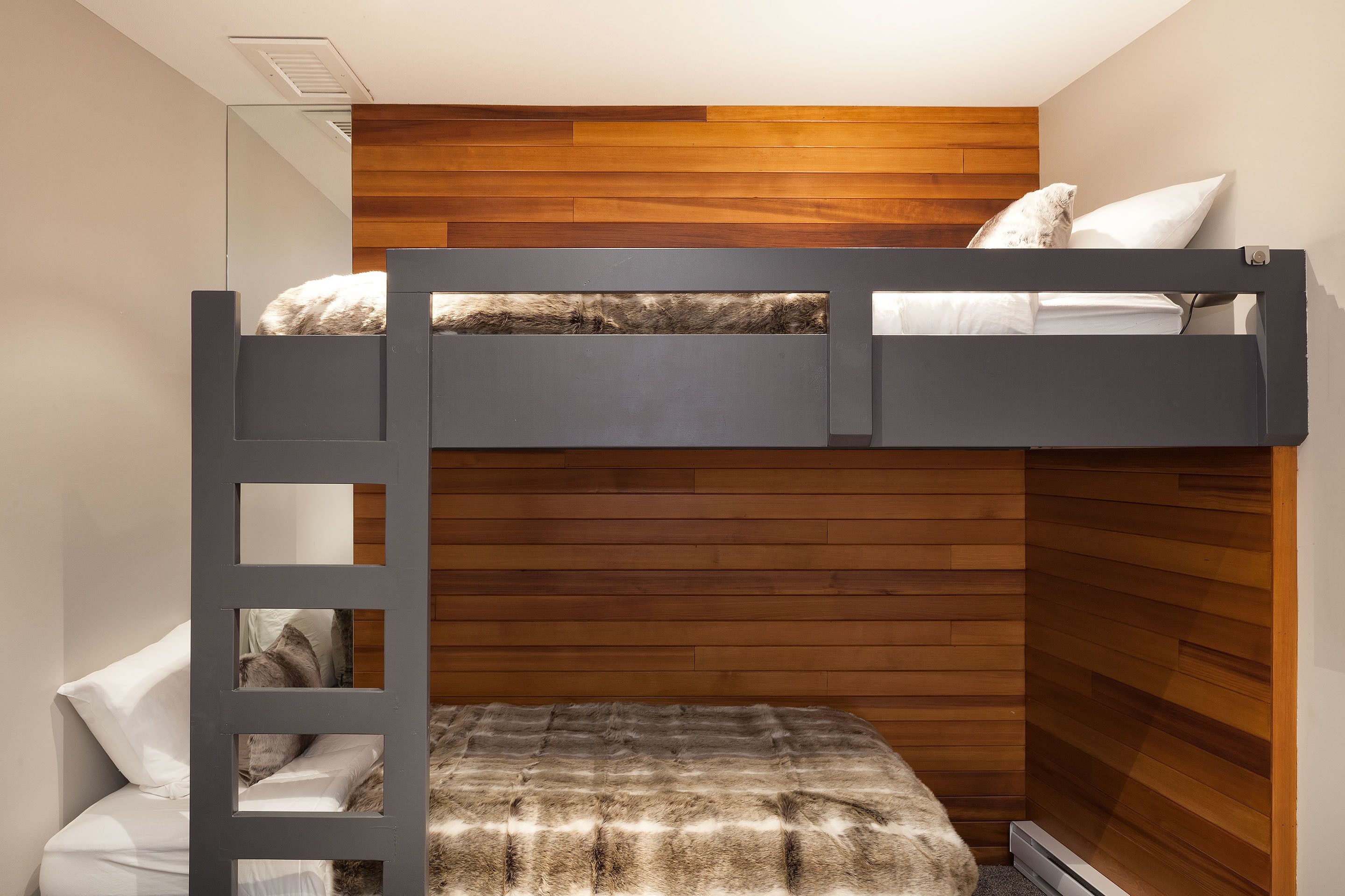 Ein Stockbett mit Holzkopfteil, einer Stehle und einer kleinen Sitzbank darunter.