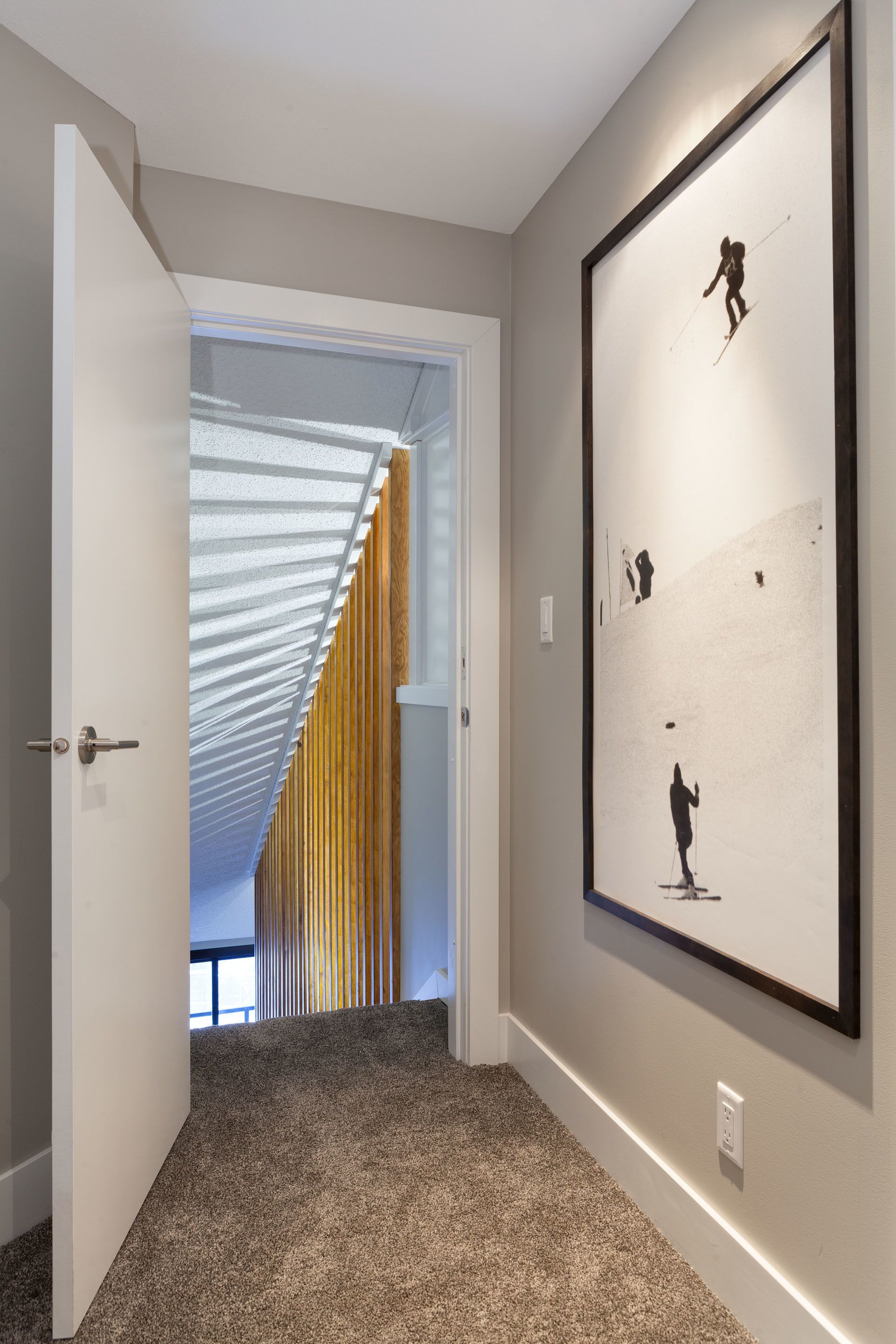 A hallway with a framed artwork on the wall, a door leading to another room, and a sloped ceiling with wooden panels.