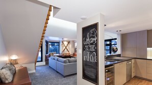 Un interior moderno con una escalera, una sala de estar con sofá, una cocina con armarios de madera y un cartel que dice 'Welcome to the Penthouse'.