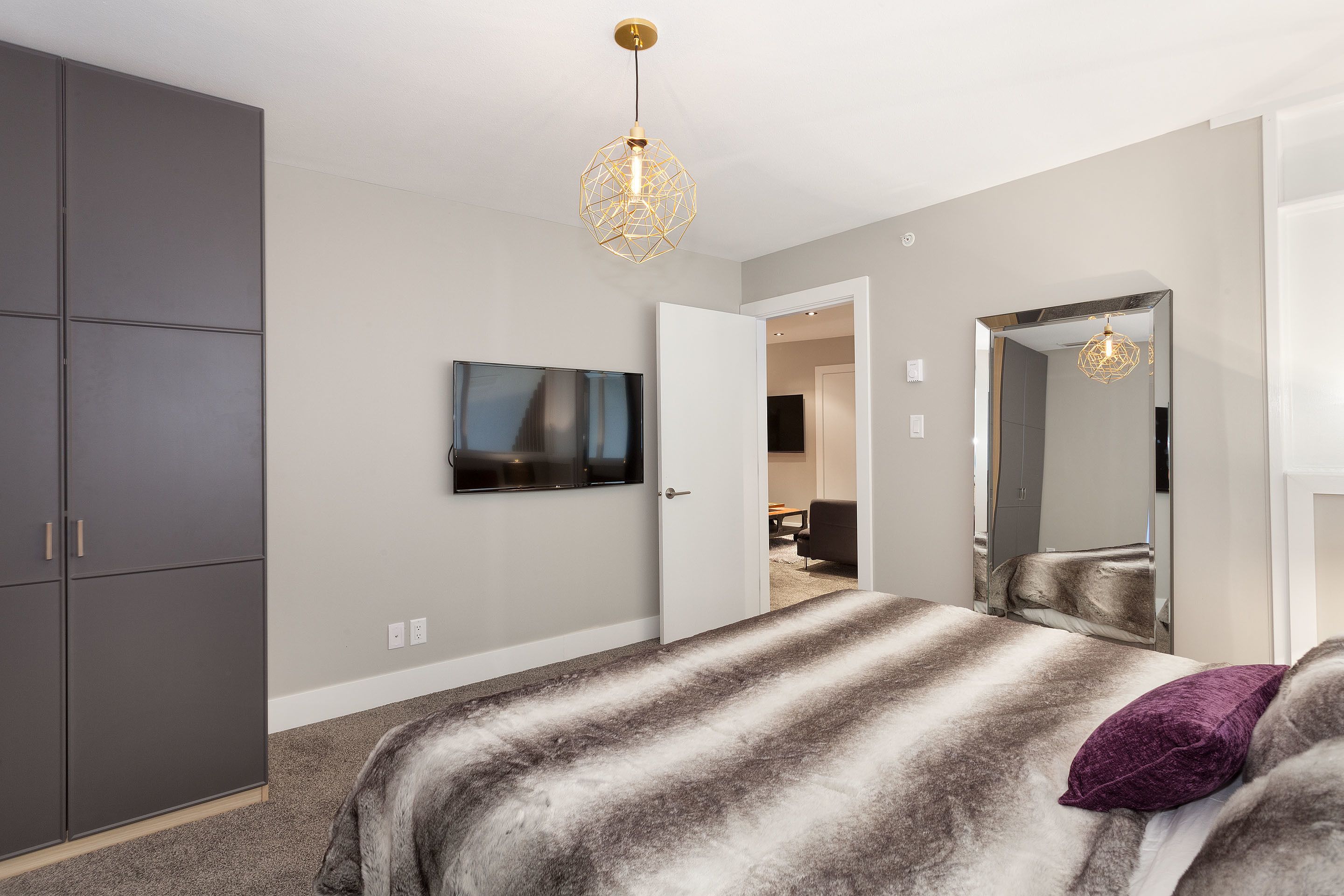 Un dormitorio con una cama grande, un televisor montado en la pared, un armario y un espejo.