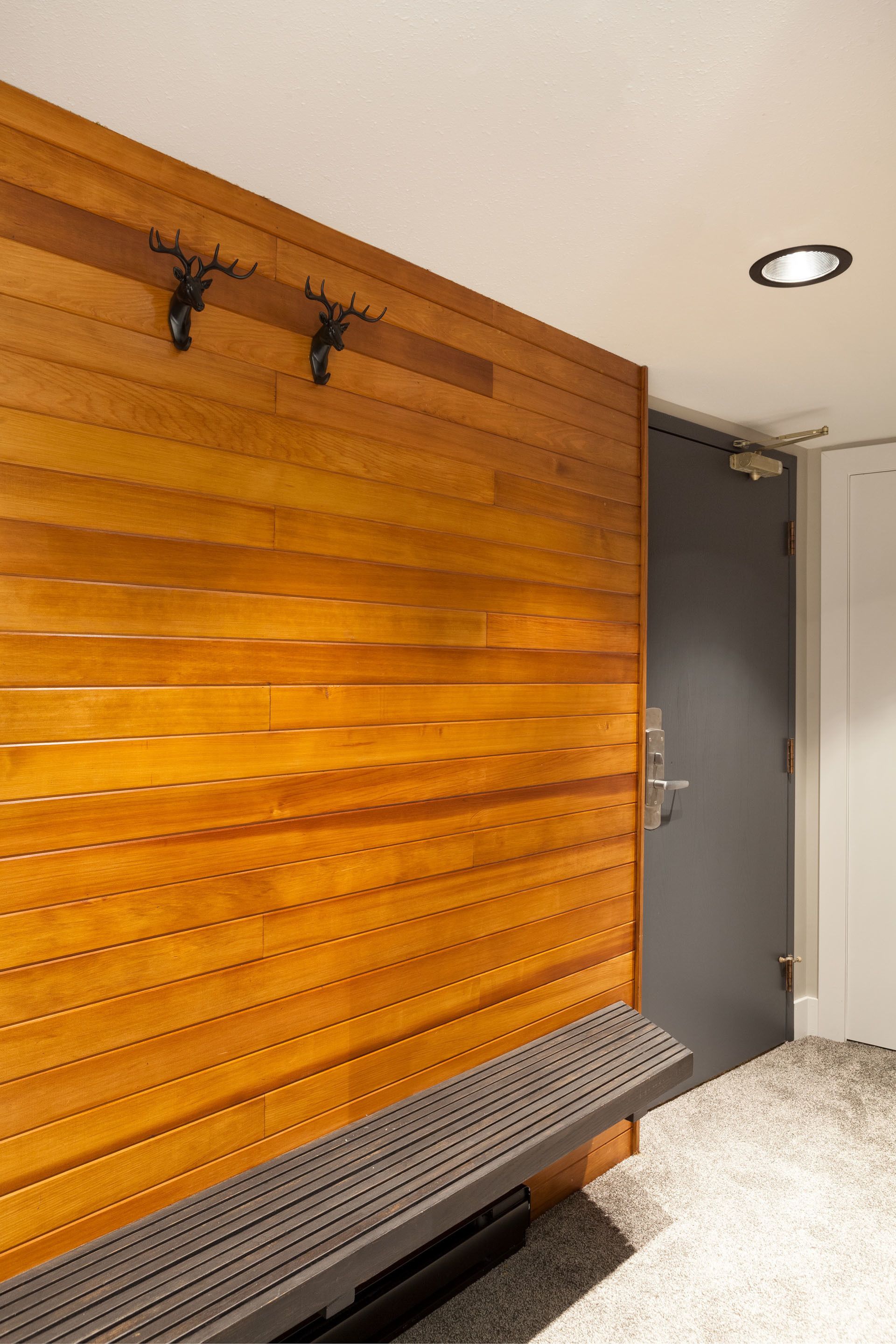 A room with a wooden panel wall, a bench, and a door.