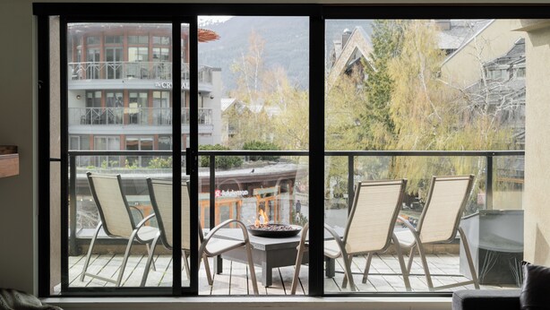 Una habitación con un amplio ventanal corredero que da a un patio exterior con sillas y una chimenea.