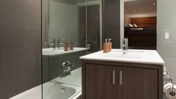 Une salle de bain moderne dotée d’une douche à parois de verre, d’une baignoire sur pieds et d’un meuble-lavabo en bois avec un plan de travail blanc.