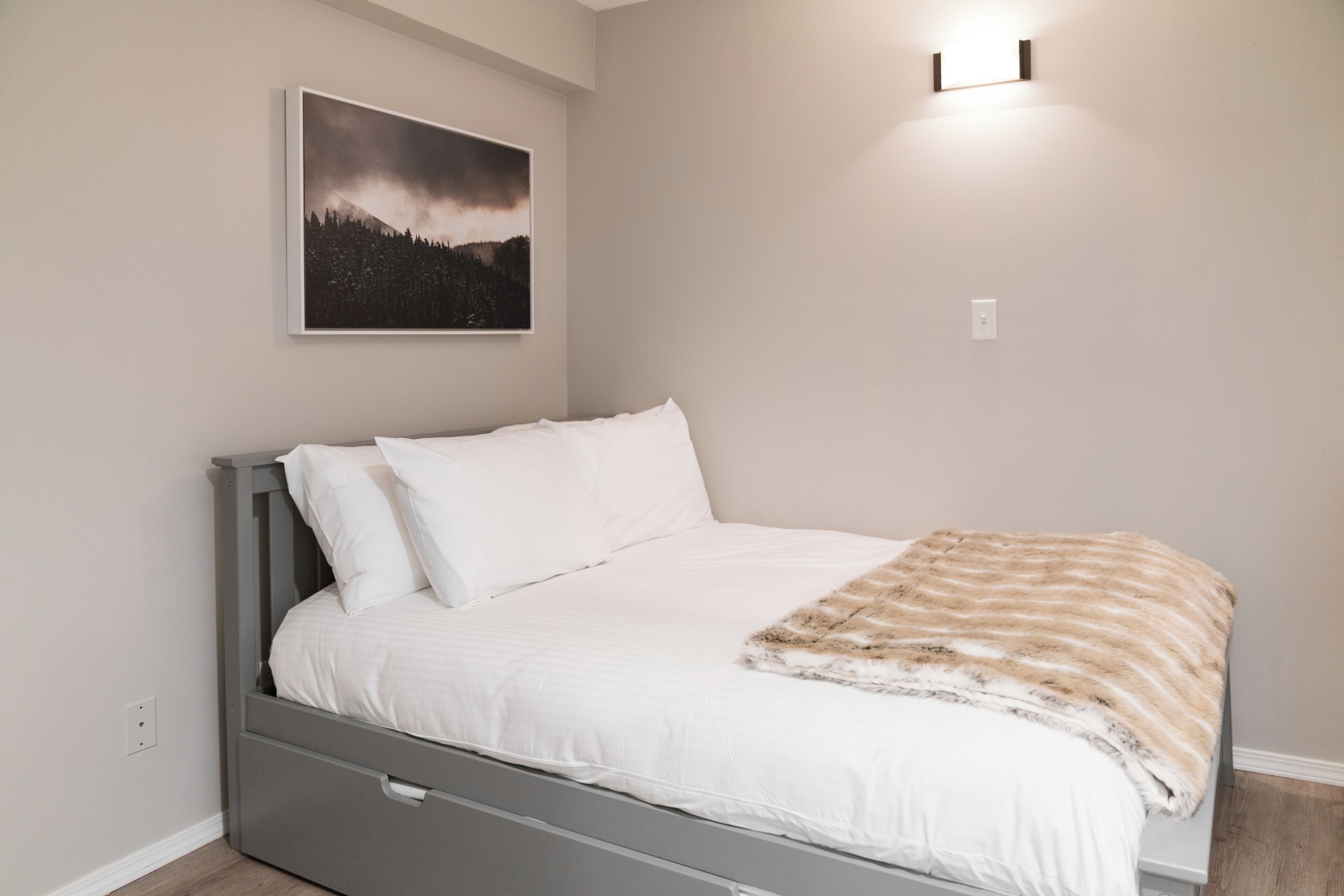 Ein Schlafzimmer mit einem Bett, einer Wandleuchte und einem gerahmten Bild.