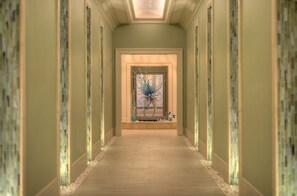 A hallway with a central door leading to a room, flanked by walls with mosaic patterns and a wooden floor.