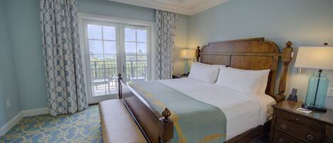 A hotel room with a large bed, a bench, a nightstand, and a view of the outdoors through a window.