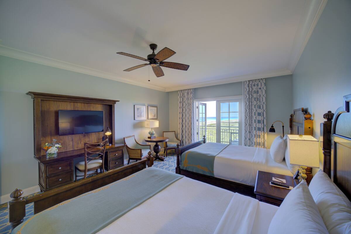 A hotel room with two beds, a desk, a chair, a television, and a balcony with a view.