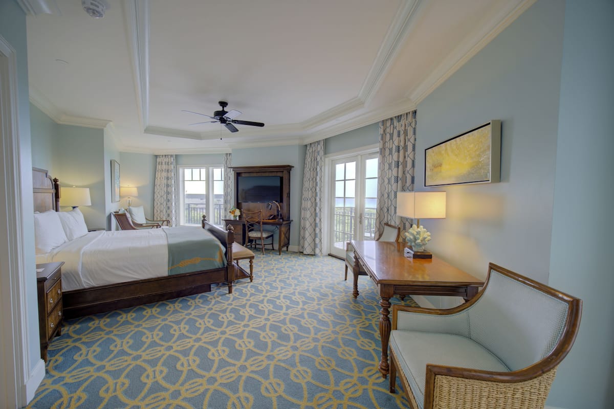 A hotel room with a large bed, a desk with a chair, a television, and a window with curtains.