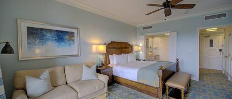 A hotel room with a bed, a sofa, a ceiling fan, and a large framed artwork on the wall.