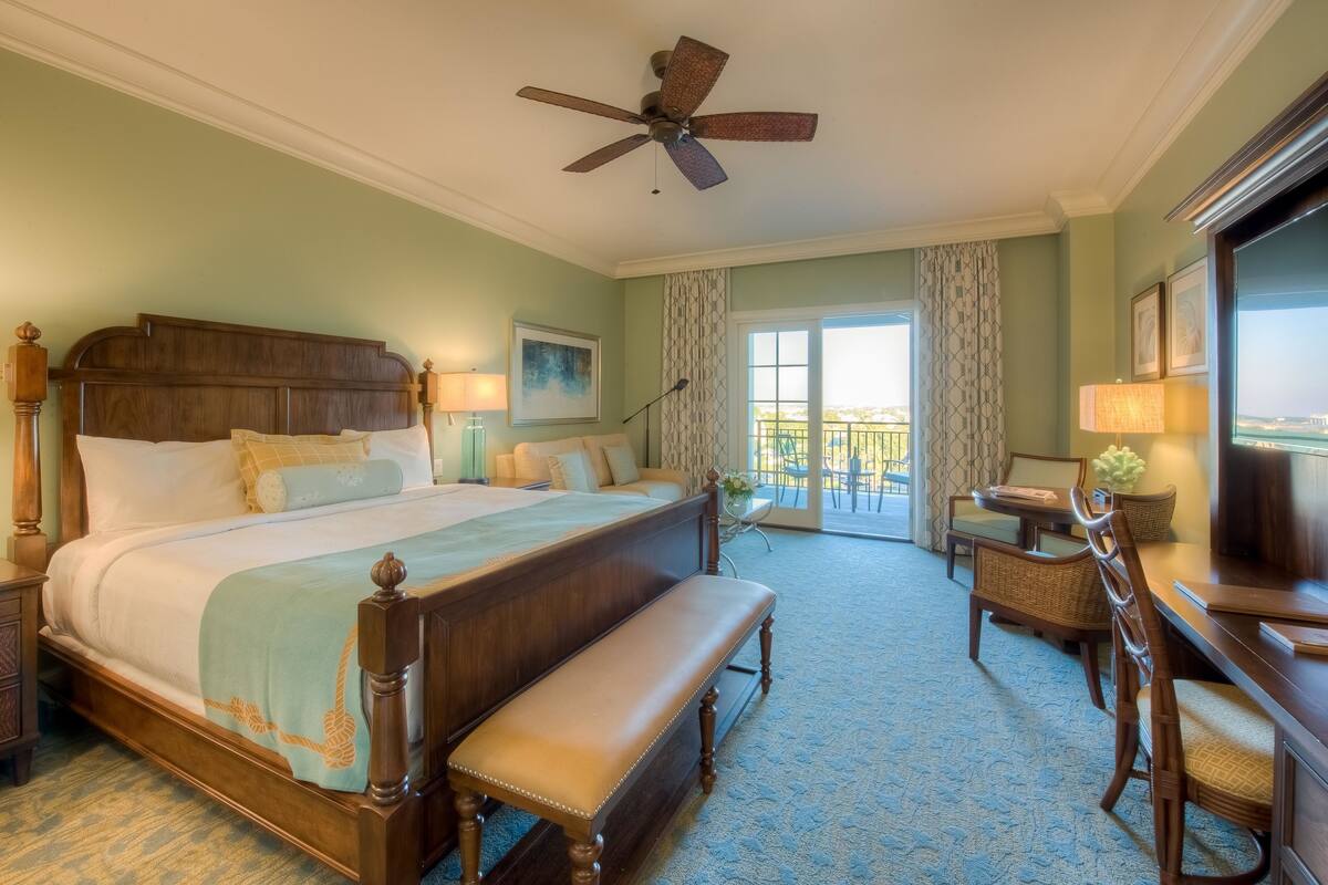 Habitación de hotel con una cama grande, un banco, un escritorio y un ventilador de techo.