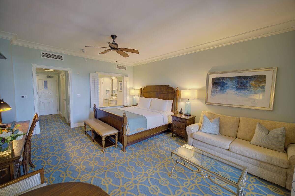 A hotel room with a bed, a sofa, a dining table, and a ceiling fan.