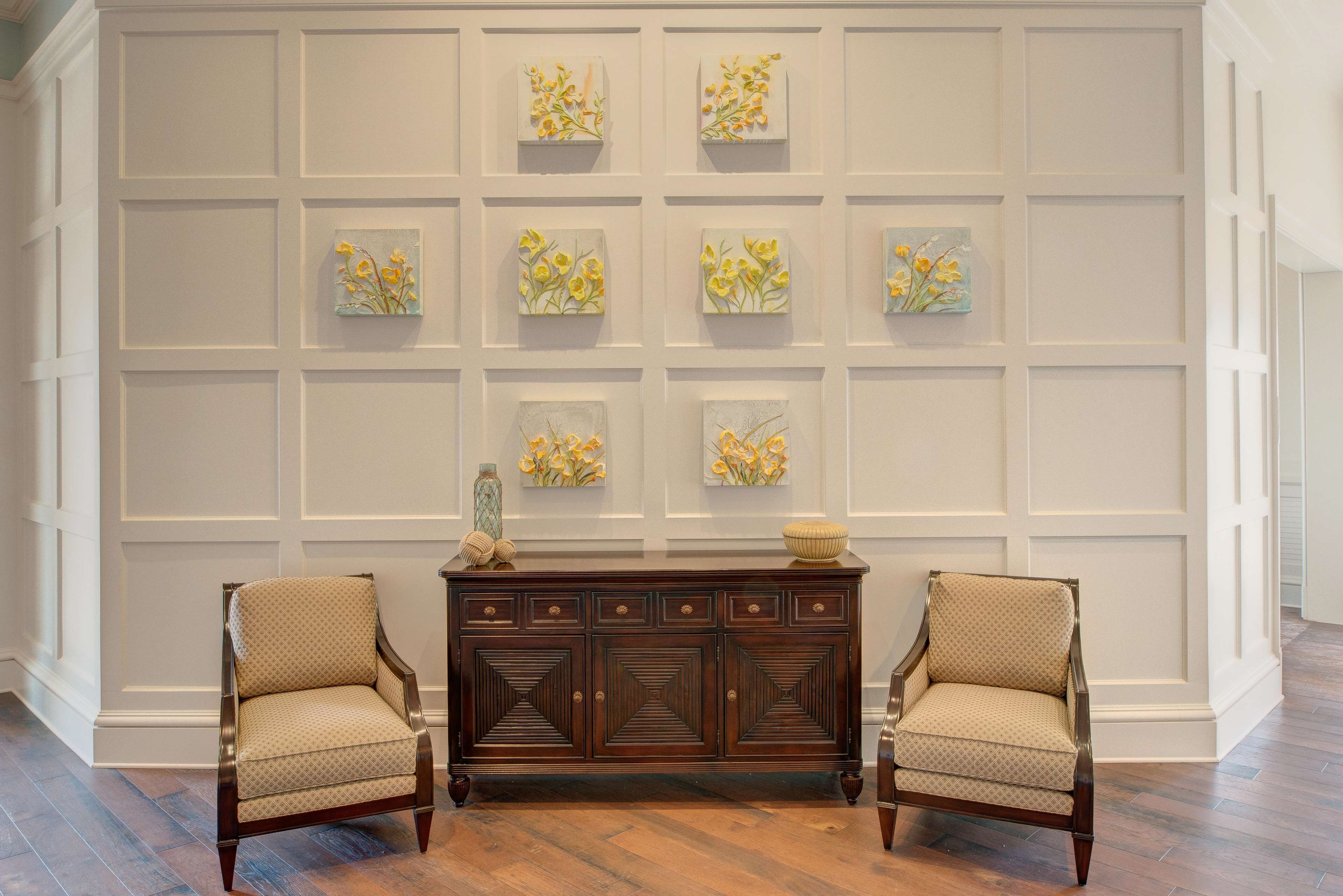 A room with a wooden cabinet, two armchairs, and a wall with framed artwork.