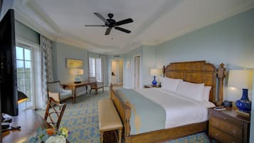 A hotel room with a large bed, a desk with a chair, a bench, a TV, and a ceiling fan.