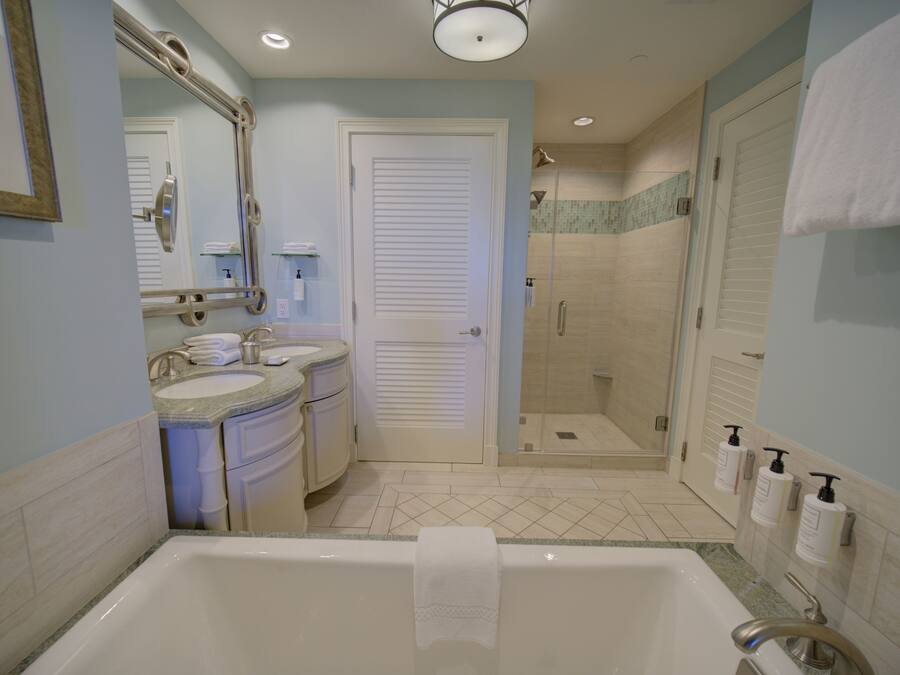 A bathroom with a bathtub, two sinks, a shower, and a door leading to another room.