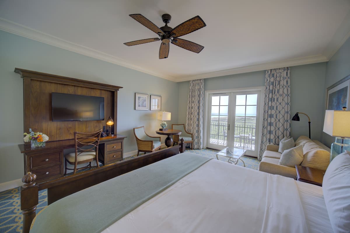 A hotel room with a large bed, a desk with a chair, a TV, and a balcony with a view.