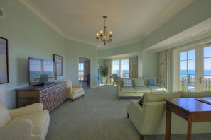 A spacious living room with a large television, comfortable seating, and a view of the ocean through the windows.