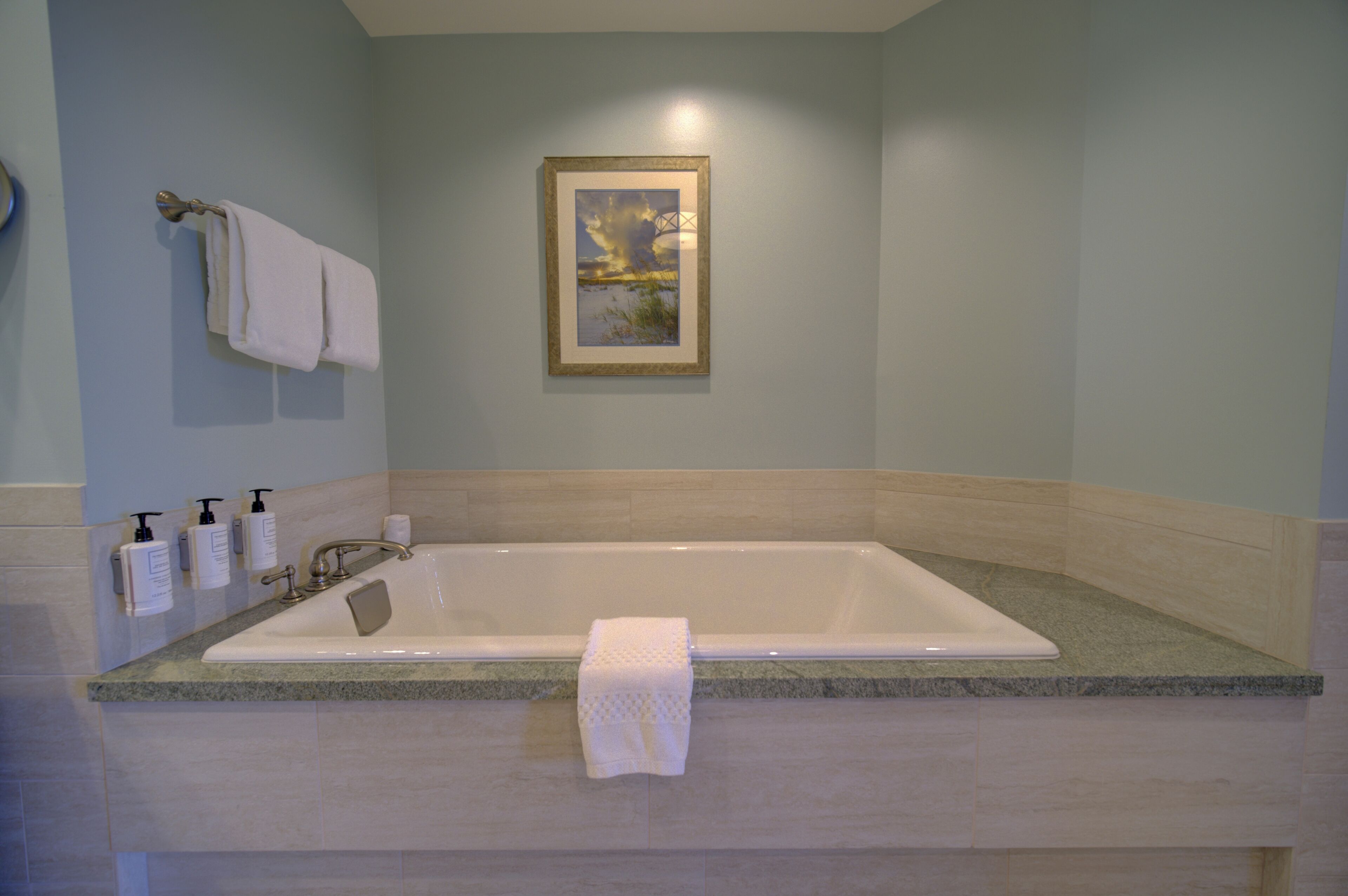 A bathroom with a large bathtub, a framed picture on the wall, and toiletries on the counter.