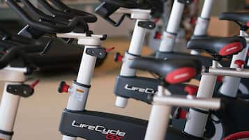 Varias bicicletas estáticas en un gimnasio, con un espejo en la pared y equipo de ejercicio al fondo.