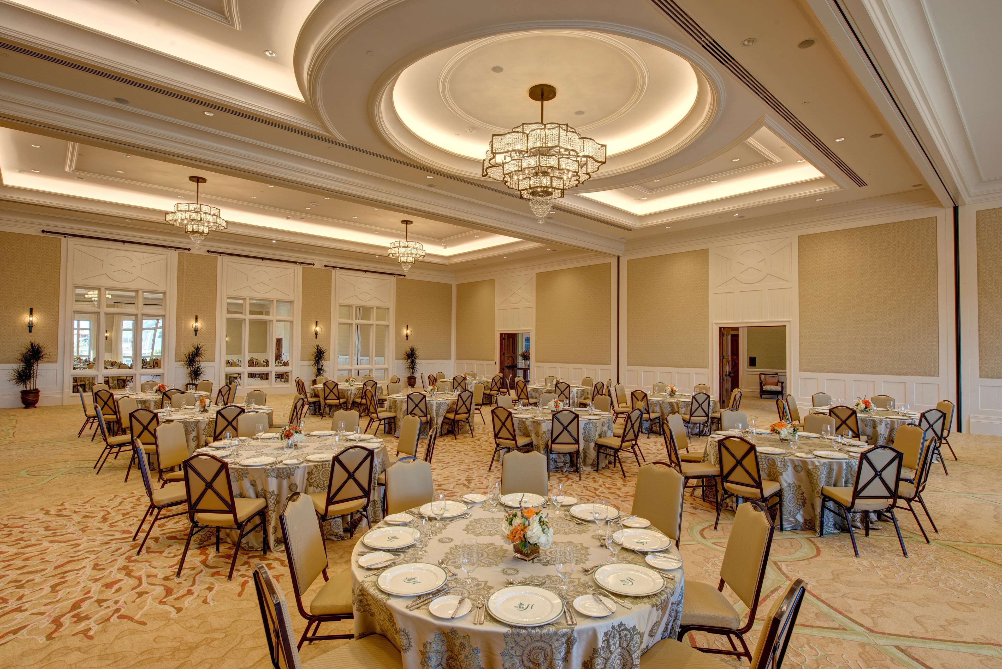 Un salón de banquetes con mesas redondas, sillas, candelabros y piso alfombrado.