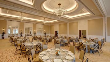 Une salle de banquet avec des tables rondes, des chaises, des lustres et un sol recouvert de moquette.