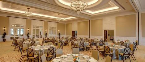 Une salle de banquet avec des tables rondes, des chaises, des lustres et un sol recouvert de moquette.