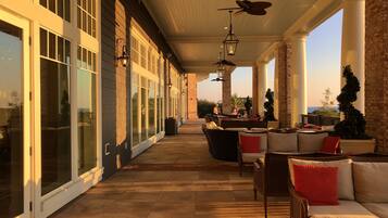 A covered outdoor seating area with large windows, a brick wall, and a view of the sea.