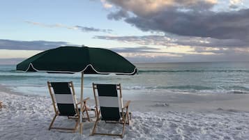 Two beach chairs under a green umbrella on a sandy beach with the ocean in the background.