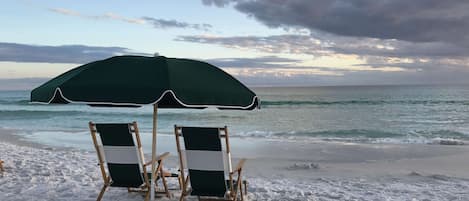 Two beach chairs under a green umbrella on a sandy beach with the ocean in the background.