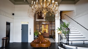A grand lobby with a chandelier, a staircase, and an elevator. - H Hotel (Los Angeles)