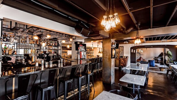 A bar area with high stools, a counter with various bottles, and hanging light fixtures. - H Hotel (Los Angeles)