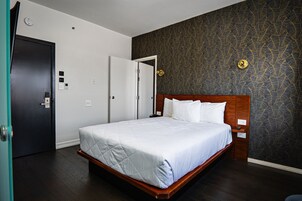 A hotel room with a bed, a door, a wall clock, and a light switch.