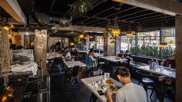 A restaurant with indoor dining, exposed brick walls, hanging plants, and pendant lighting.