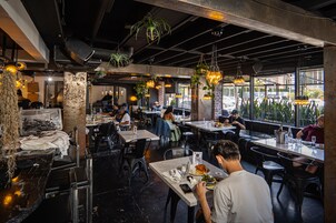Un ristorante con sala interna, pareti in mattoni a vista, piante pensili e luci a sospensione.