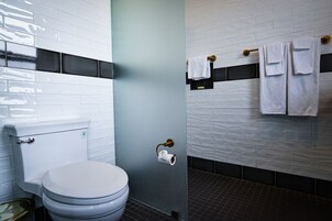 A modern bathroom with a toilet, a glass shower enclosure, and a towel rack with multiple towels.