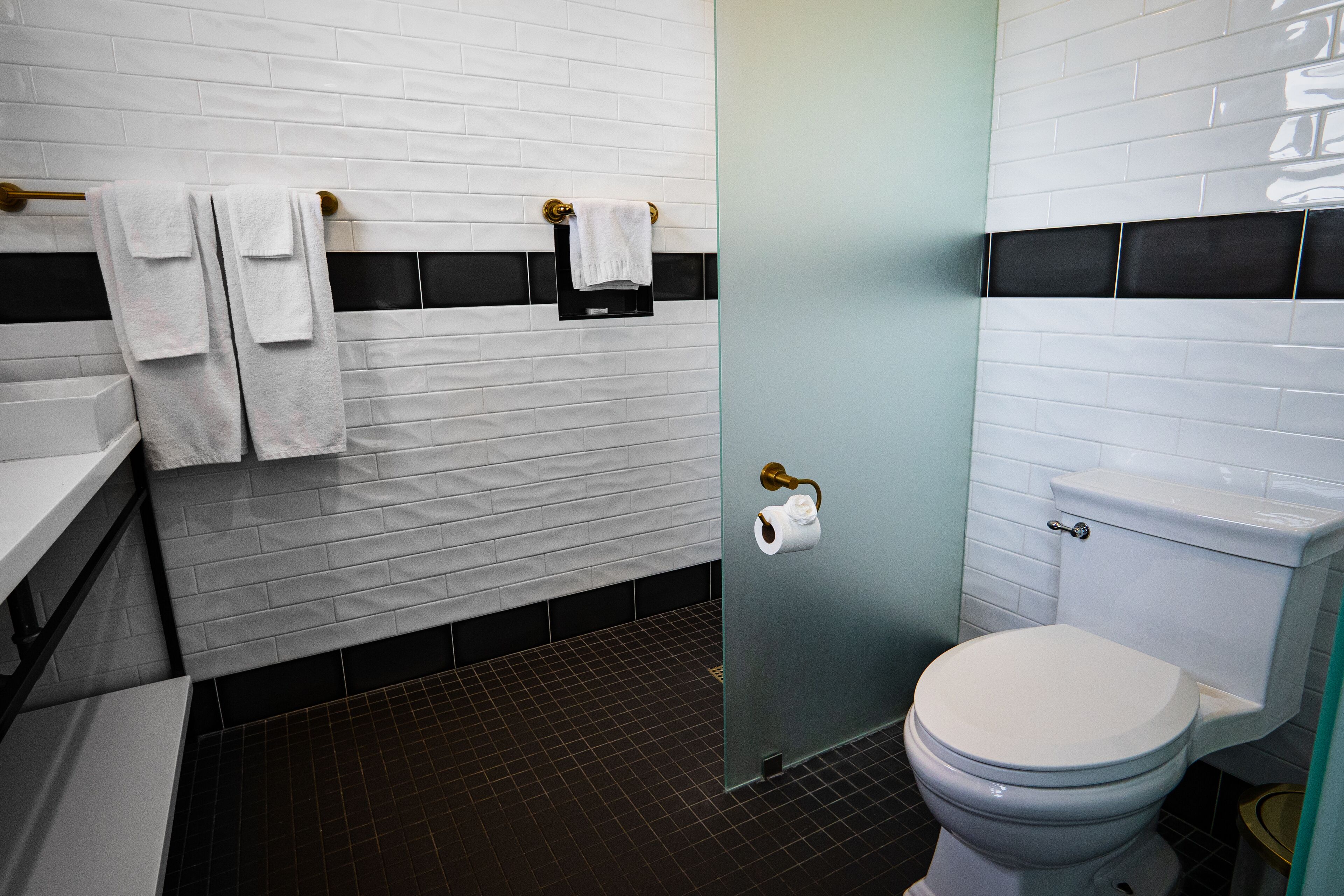 Ein Badezimmer mit weißen Ziegelstreifenfliesen, einem schwarz-weißen Duschbereich, einer weißen Toilette und einem Handtuchhalter mit Handtüchern.