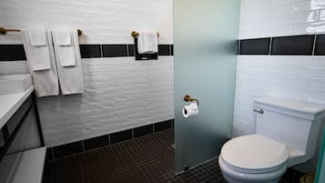 Ein Badezimmer mit weißen Ziegelstreifenfliesen, einem schwarz-weißen Duschbereich, einer weißen Toilette und einem Handtuchhalter mit Handtüchern.