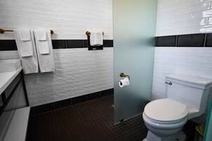 Een badkamer met witte metrotegels, een douchegedeelte met zwart-witte tegels, een wit toilet en een handdoekrek met handdoeken.