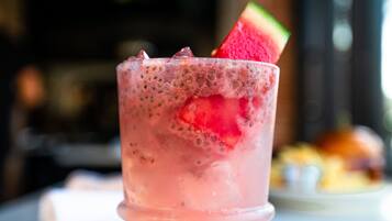 Un verre contenant une boisson rose, orné d’une tranche de pastèque sur le bord, posé sur une surface en marbre.