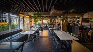 A modern restaurant interior with a long counter, booths, and hanging plants. - H Hotel (Los Angeles)